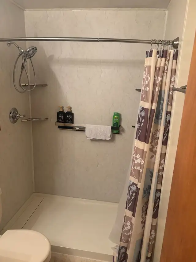 Shower replacement with beige stone-look walls, low-threshold base, grab bar and corner caddy