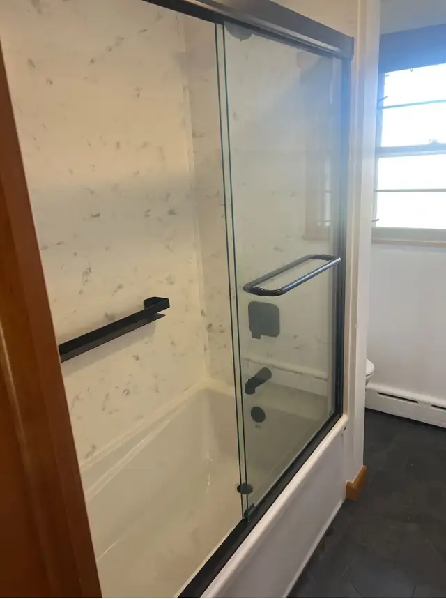 Bathtub replacement with marble-look solid surface surround and sliding glass doors with black hardware