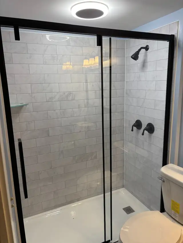 Walk-in shower with gray subway-look walls, matte black fixtures and a black-framed sliding glass door