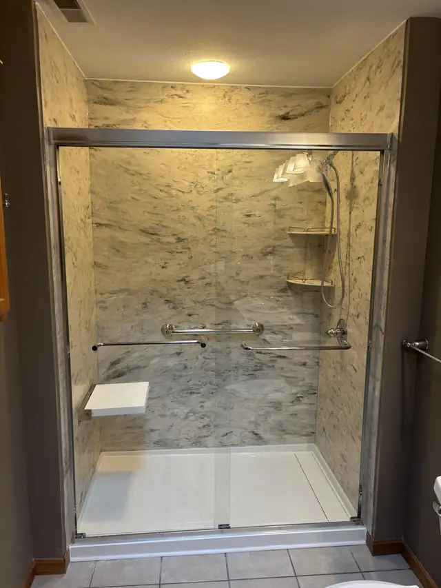 Tub to shower conversion in Lowellville, Ohio with marble-look walls, fold-down seat, grab bar and sliding glass door