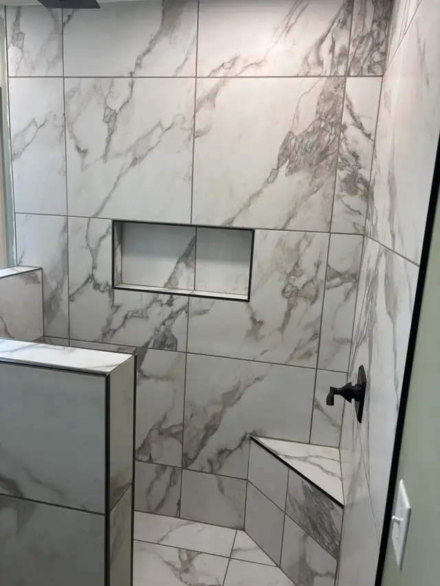 Custom tile shower with large marble-look tile, a recessed niche, built-in corner bench and black shower valve
