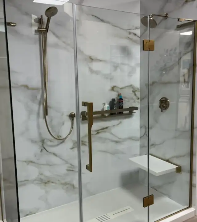 Walk-in shower with marble-look solid surface walls, a frameless glass door, brushed brass fixtures and a fold-down seat